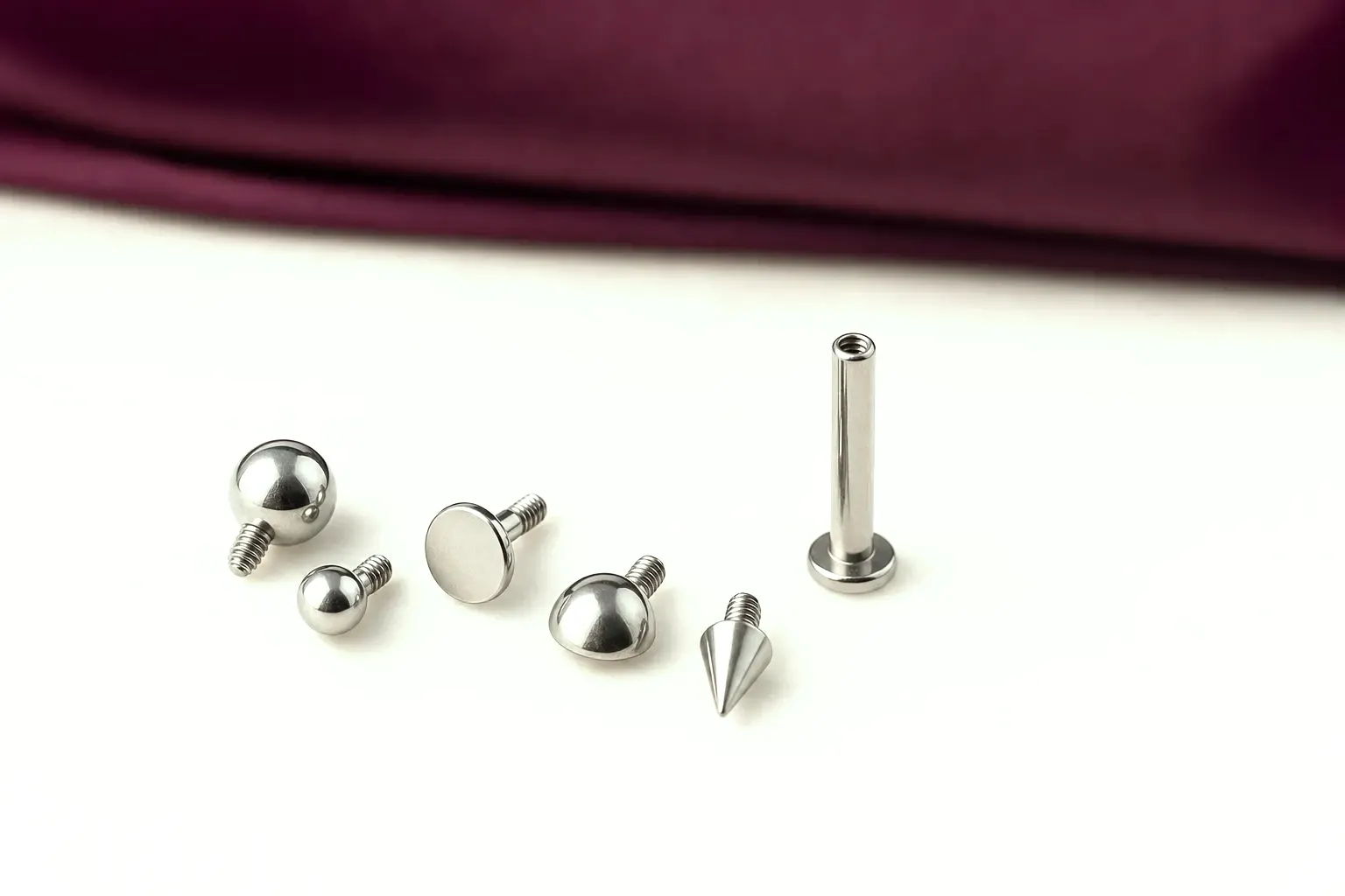 Fünf silberfarbene Aufsätze — Kugeln, flache Scheibe, Kuppel und Kegel — neben einem Labret-Stab