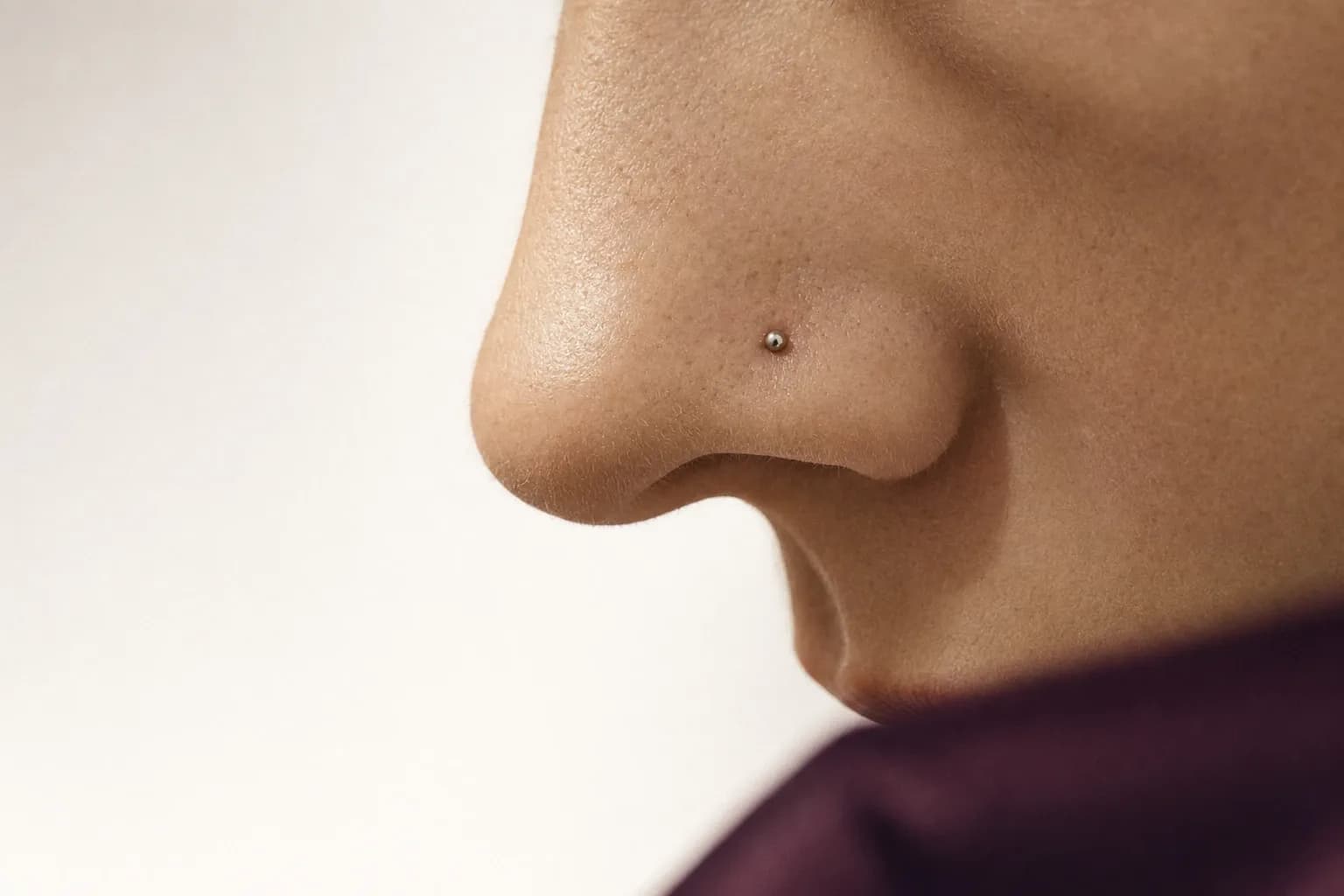 Nase im Profil mit einem kleinen silberfarbenen Stecker im Nasenflügel vor hellem Grund